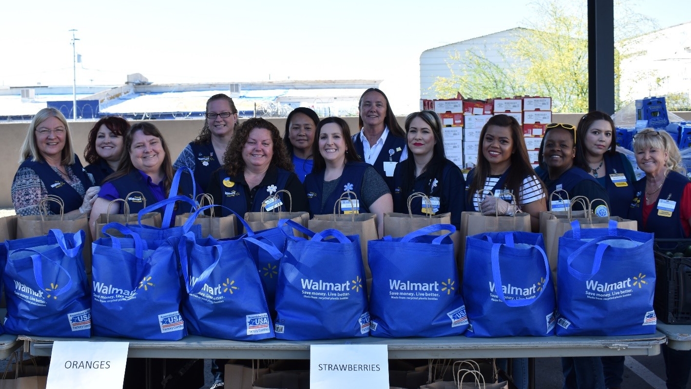 Photo of group of associates standing behind a table full of Walmart blue bags filled with donation items.